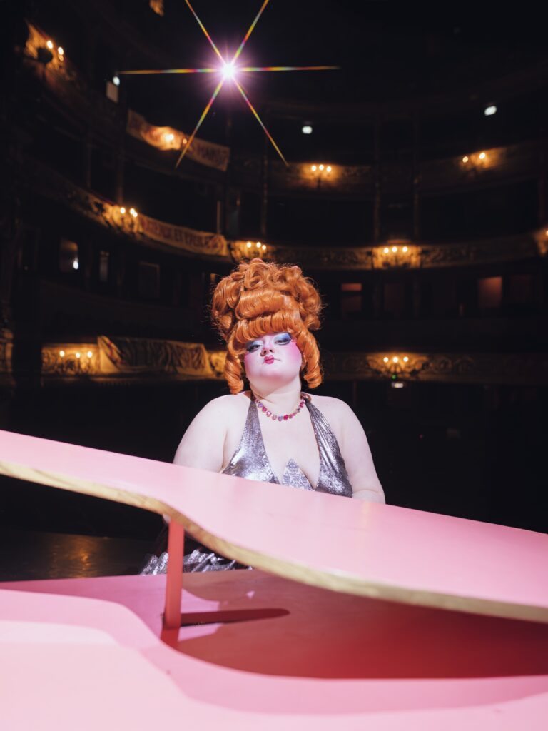 Madeleine Flamboyante lors d’un numéro musical du spectacle drag Topcoat, pleine d’énergie et de paillettes.